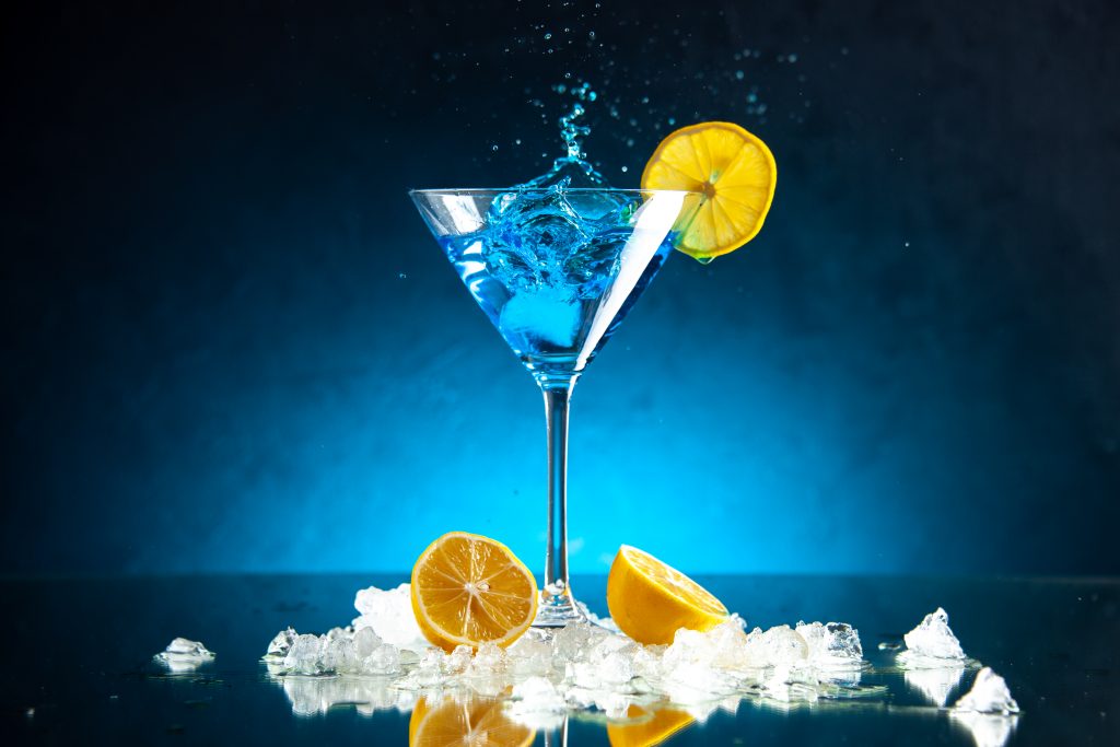 A blue cocktail decorated with lemon and ice.