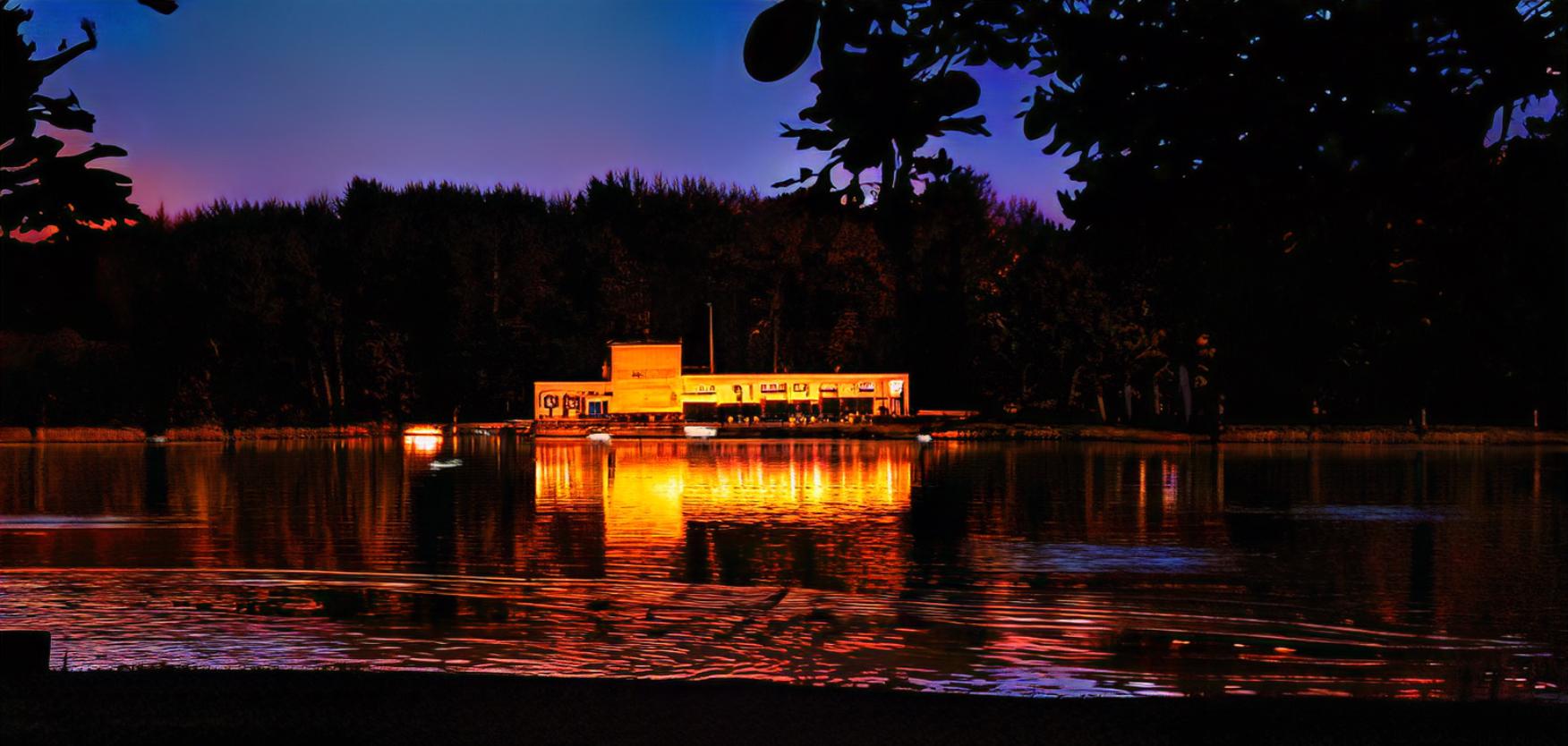 a photograph of lairds table at night. It shows the building lit up viewed from across the lake.