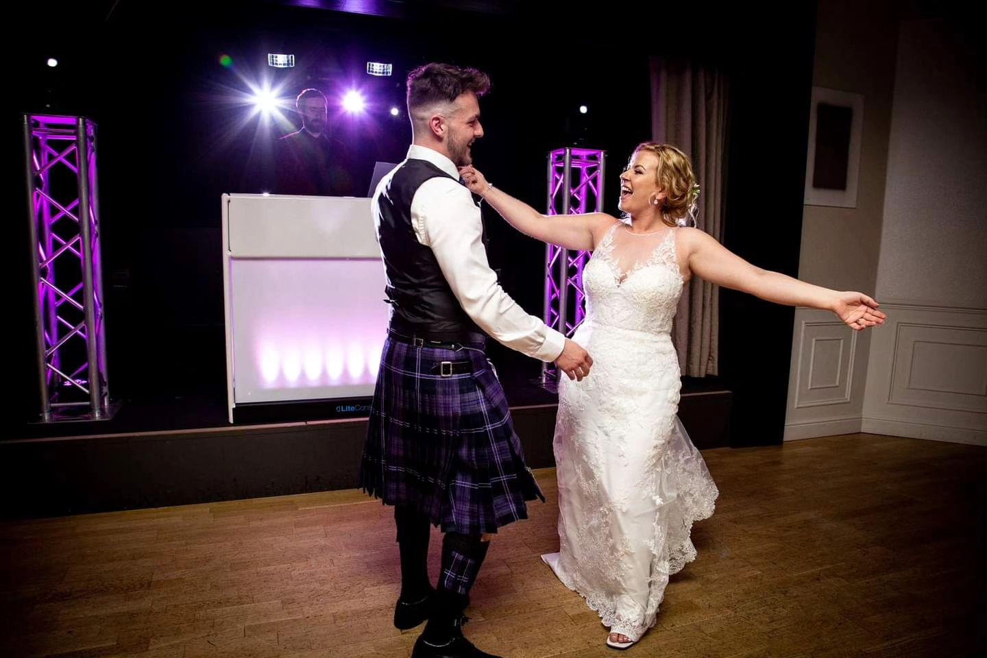 a bride and groom dance on a dancefloor with a dj in the background